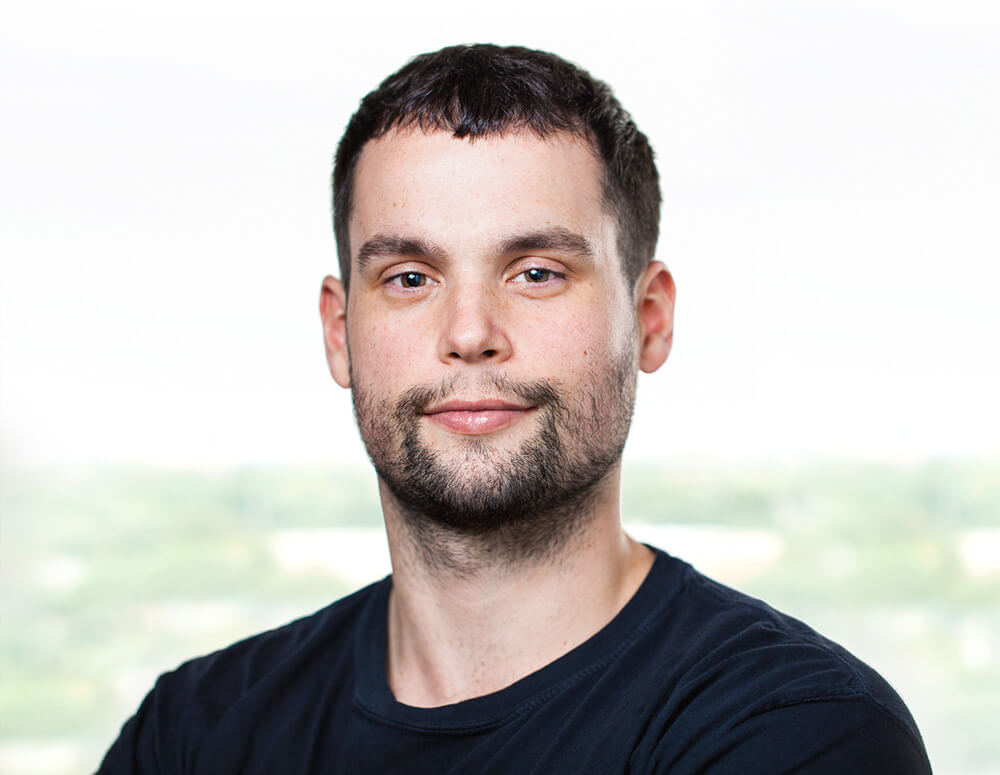 A casual man with a light beard smiling against a bright background.