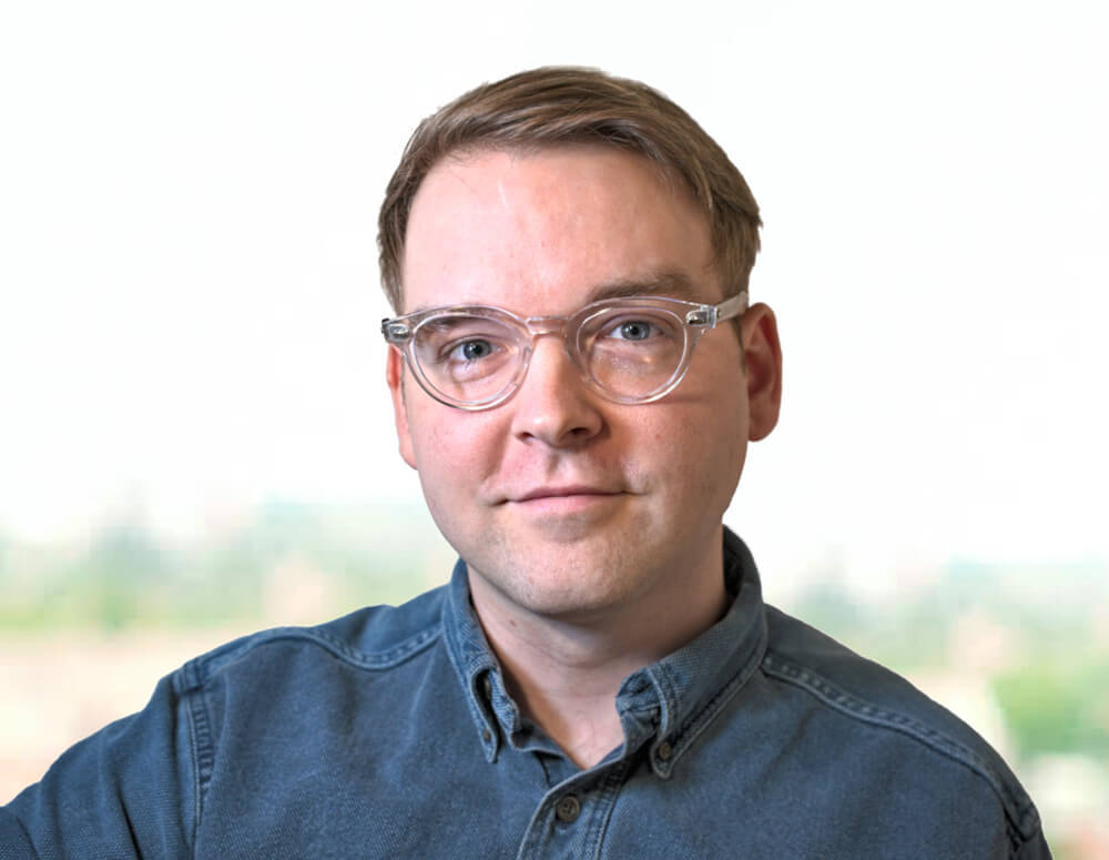 A man with glasses standing in front of a window.